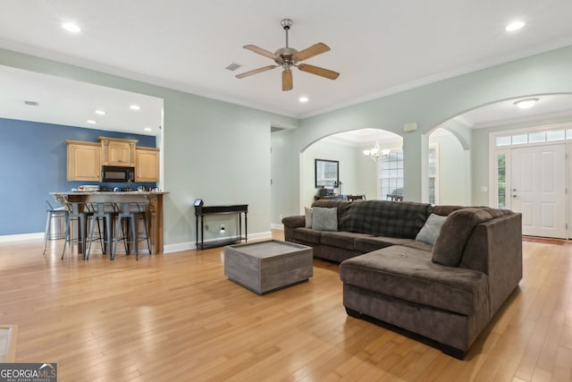 living room with ornamental molding, ceiling fan with notable chandelier, and light hardwood / wood-style floors