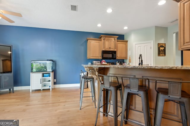 kitchen featuring light wood-type flooring, light stone countertops, ceiling fan, and a breakfast bar