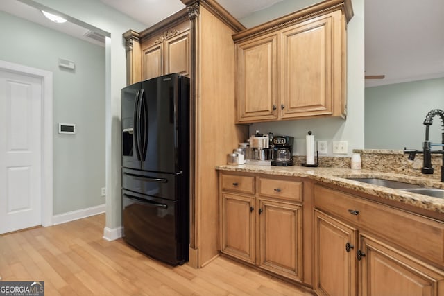 kitchen with light stone countertops, black fridge with ice dispenser, sink, and light hardwood / wood-style flooring