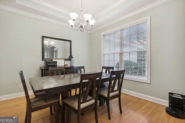 dining room with a notable chandelier, wood-type flooring, a raised ceiling, and crown molding