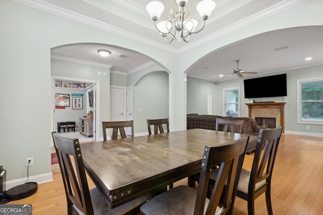 dining room with crown molding, a fireplace, ceiling fan with notable chandelier, and light hardwood / wood-style flooring