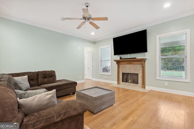 living room with light wood-type flooring, a tile fireplace, and crown molding