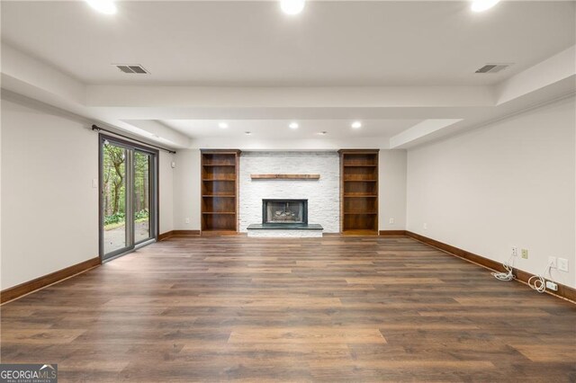 unfurnished living room featuring dark hardwood / wood-style floors, a tray ceiling, and a stone fireplace