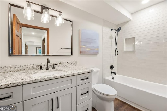 full bathroom with wood-type flooring, tiled shower / bath, vanity, and toilet