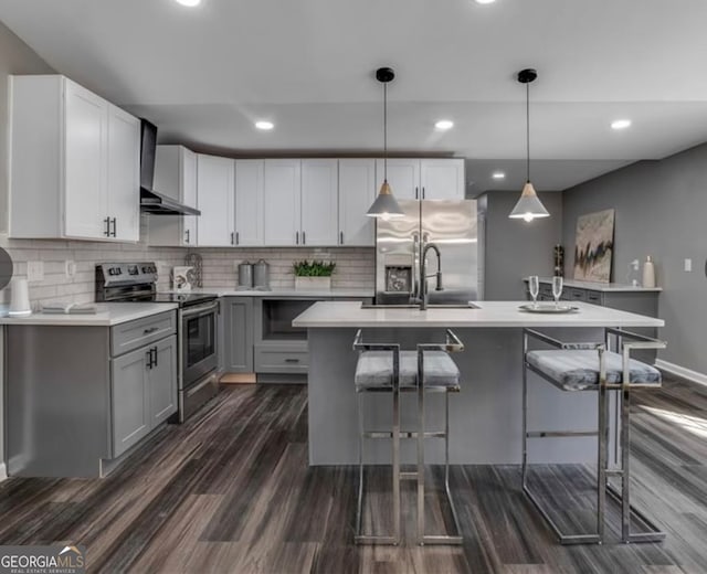 kitchen with an island with sink, wall chimney exhaust hood, pendant lighting, and stainless steel appliances