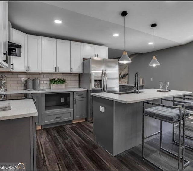 kitchen featuring an island with sink, hanging light fixtures, sink, dark hardwood / wood-style flooring, and decorative backsplash