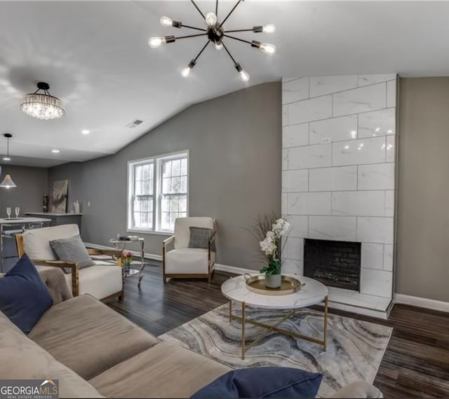 living room with a notable chandelier, lofted ceiling, a tile fireplace, and dark wood-type flooring