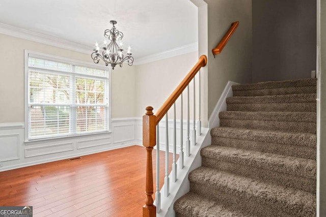 stairway with crown molding, hardwood / wood-style floors, and a chandelier