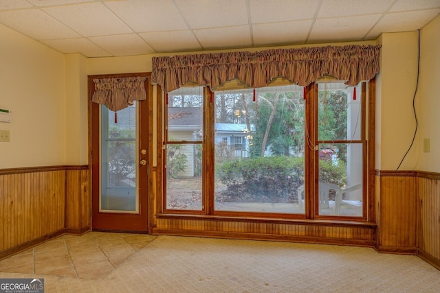 doorway featuring a drop ceiling, a healthy amount of sunlight, and wood walls