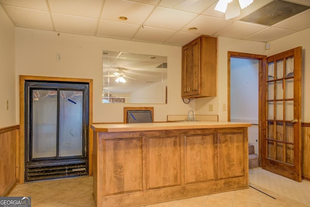 kitchen featuring kitchen peninsula, a paneled ceiling, ceiling fan, wooden walls, and sink