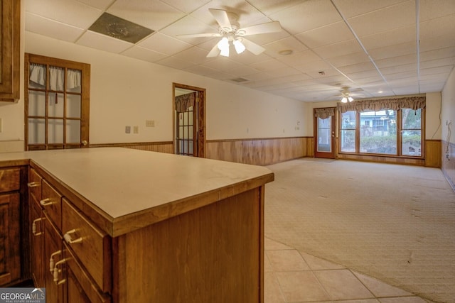 kitchen featuring light carpet, a drop ceiling, wooden walls, and ceiling fan