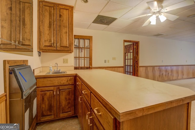 kitchen featuring a drop ceiling, kitchen peninsula, sink, and wooden walls