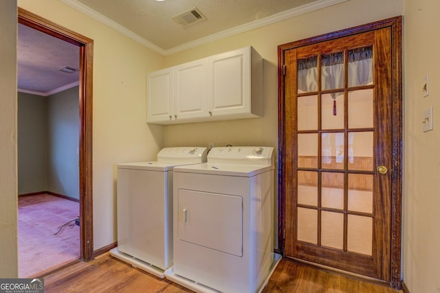 clothes washing area with cabinets, wood-type flooring, washer and dryer, and ornamental molding