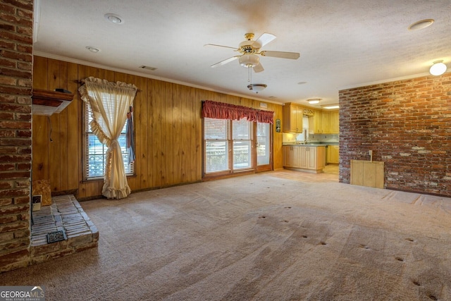 unfurnished living room featuring wood walls, sink, ceiling fan, ornamental molding, and light colored carpet