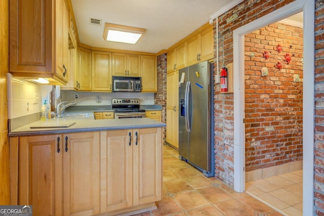 kitchen featuring sink, stainless steel appliances, brick wall, kitchen peninsula, and light tile patterned flooring