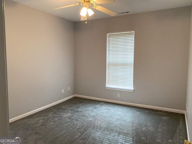 spare room featuring dark colored carpet, ceiling fan, and a wealth of natural light