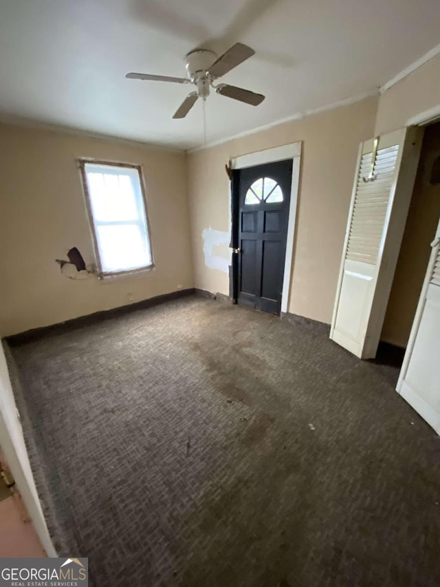 entryway featuring ceiling fan, ornamental molding, and dark colored carpet