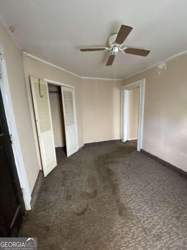 unfurnished bedroom featuring ceiling fan, a closet, crown molding, and dark carpet