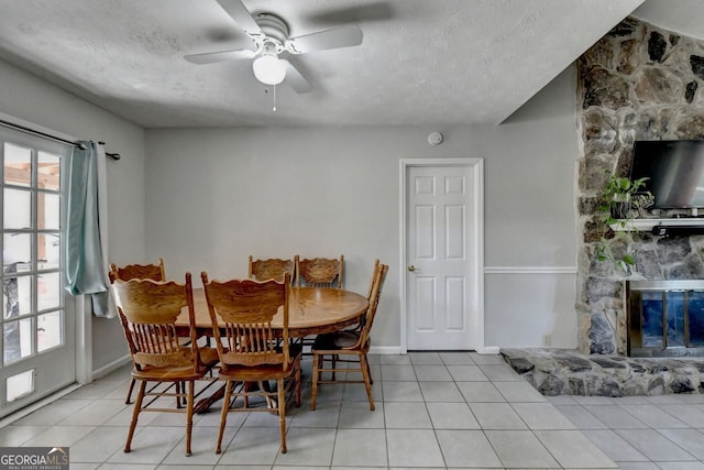 dining room featuring ceiling fan, a textured ceiling, light tile patterned flooring, and a fireplace