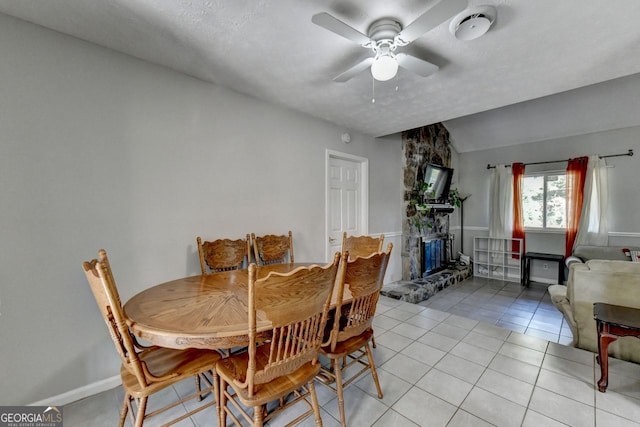 tiled dining area with vaulted ceiling, a textured ceiling, a fireplace, and ceiling fan