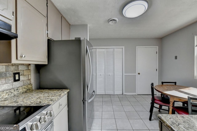 kitchen with tasteful backsplash, light stone countertops, light tile patterned flooring, and appliances with stainless steel finishes