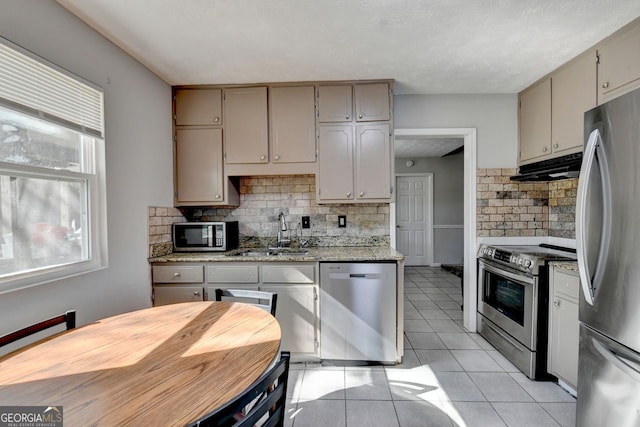 kitchen with decorative backsplash, light tile patterned floors, light stone countertops, sink, and stainless steel appliances