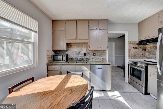 kitchen featuring appliances with stainless steel finishes, sink, light tile patterned flooring, backsplash, and light stone counters