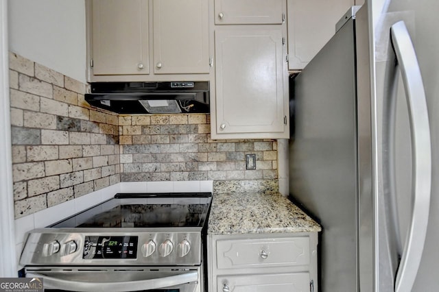 kitchen with white cabinets, light stone counters, stainless steel appliances, and backsplash