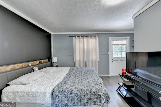 bedroom with light hardwood / wood-style flooring, a textured ceiling, and crown molding