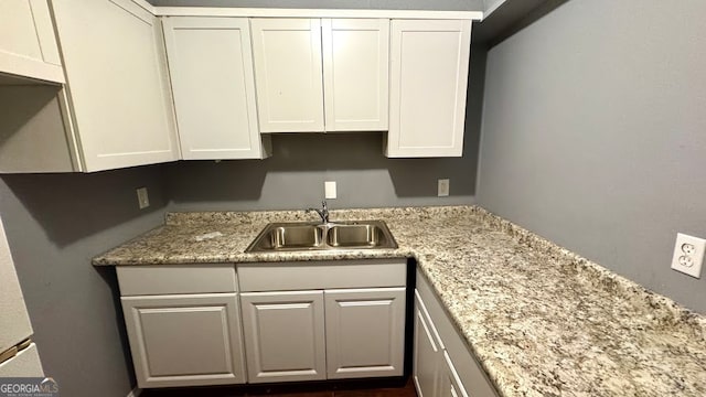 kitchen with light stone countertops, white cabinetry, and sink