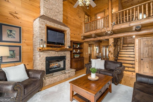 living room with a stone fireplace, wooden walls, light hardwood / wood-style flooring, and a high ceiling