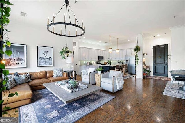 living room with crown molding, dark hardwood / wood-style flooring, sink, and a notable chandelier