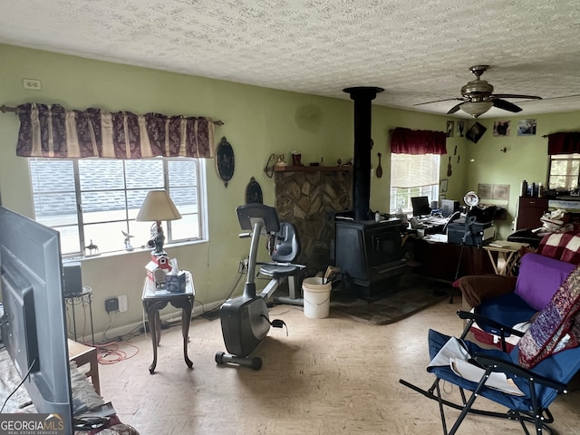 misc room featuring a textured ceiling, a healthy amount of sunlight, ceiling fan, and a wood stove