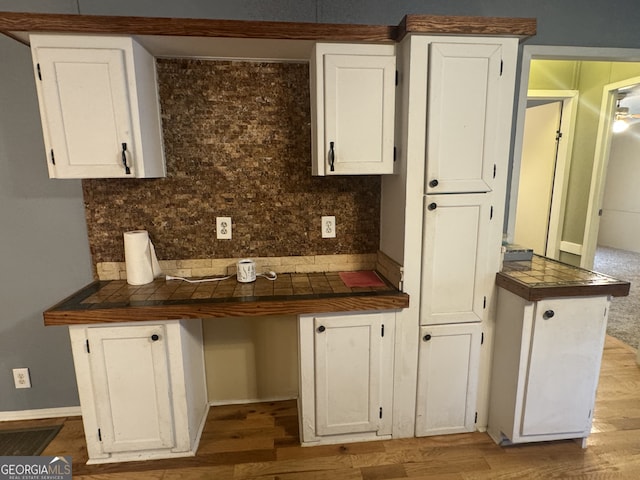 kitchen with light wood-type flooring, white cabinets, kitchen peninsula, decorative backsplash, and tile countertops