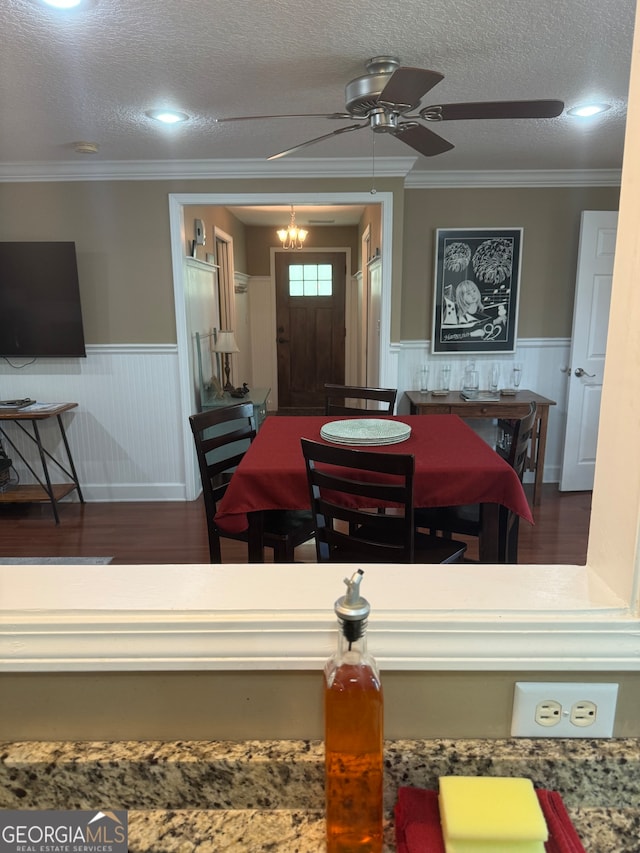 dining space with a textured ceiling, ceiling fan with notable chandelier, crown molding, and dark wood-type flooring