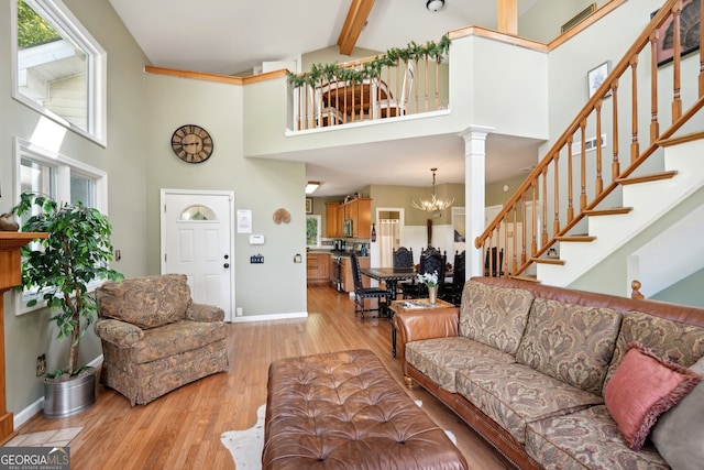 living room featuring beamed ceiling, decorative columns, a high ceiling, an inviting chandelier, and light wood-type flooring