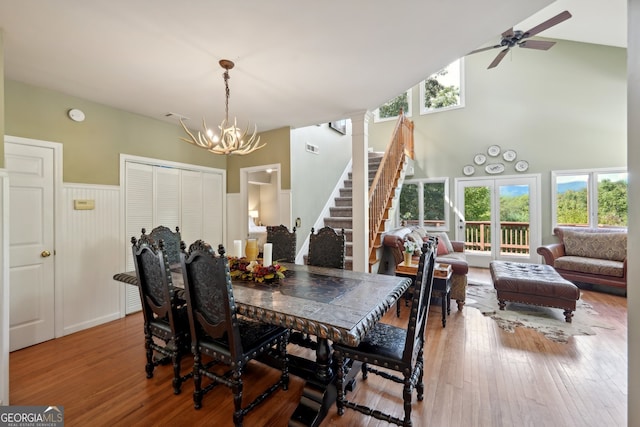 dining space with wood-type flooring, ceiling fan with notable chandelier, high vaulted ceiling, and plenty of natural light