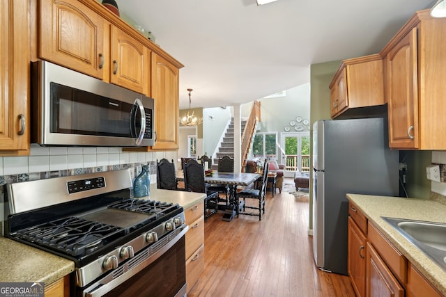 kitchen featuring tasteful backsplash, sink, light hardwood / wood-style flooring, appliances with stainless steel finishes, and decorative light fixtures