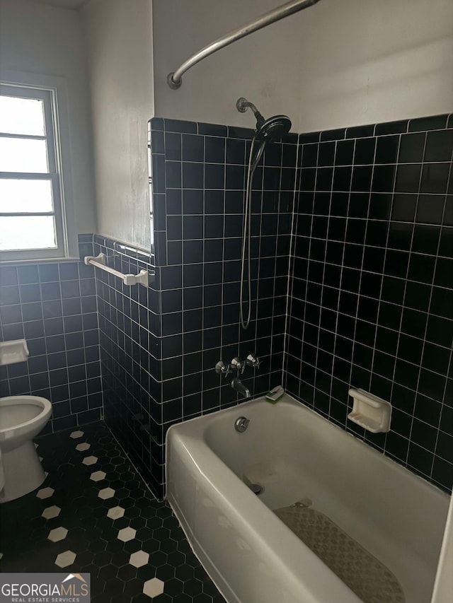 bathroom with tile walls, tile patterned floors, tiled shower / bath, and toilet