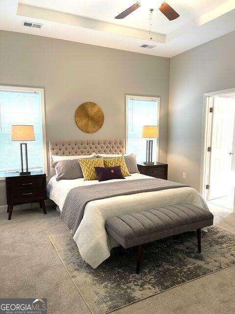 carpeted bedroom with a raised ceiling and ceiling fan