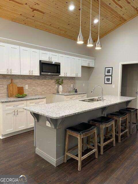 kitchen featuring wooden ceiling, a kitchen island with sink, sink, and white cabinets