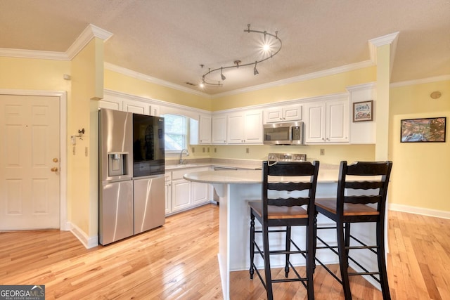 kitchen featuring white cabinets, a kitchen bar, light hardwood / wood-style flooring, stainless steel appliances, and ornamental molding