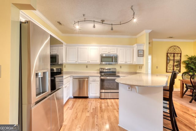 kitchen featuring a breakfast bar, white cabinets, light hardwood / wood-style floors, and appliances with stainless steel finishes