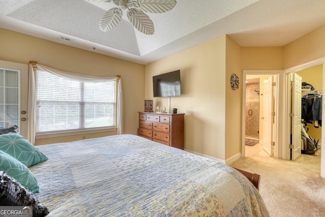 carpeted bedroom with ceiling fan, a textured ceiling, connected bathroom, and a walk in closet