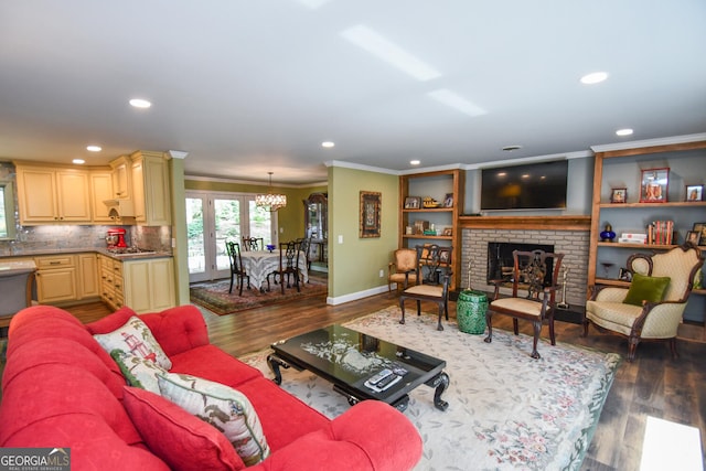 living room with ornamental molding, french doors, dark wood-type flooring, a notable chandelier, and a fireplace