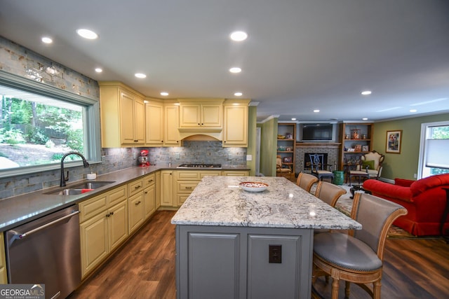 kitchen featuring stainless steel dishwasher, a brick fireplace, dark wood-type flooring, a breakfast bar area, and light stone countertops