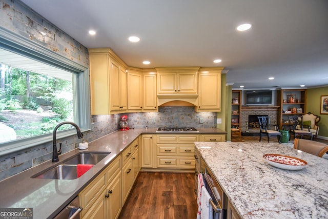 kitchen featuring sink, stainless steel gas cooktop, dark wood-type flooring, a fireplace, and light stone countertops