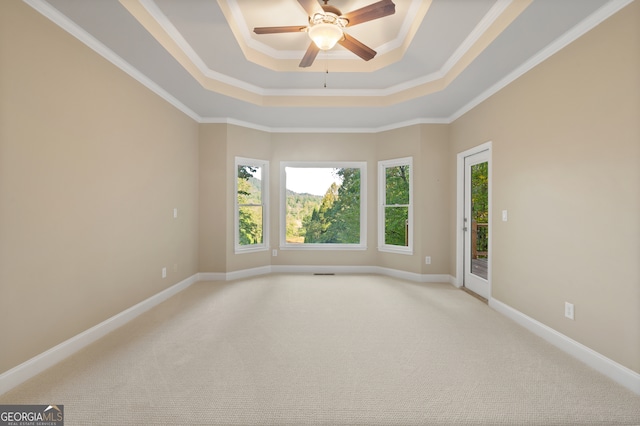 empty room with a raised ceiling, light carpet, crown molding, and ceiling fan