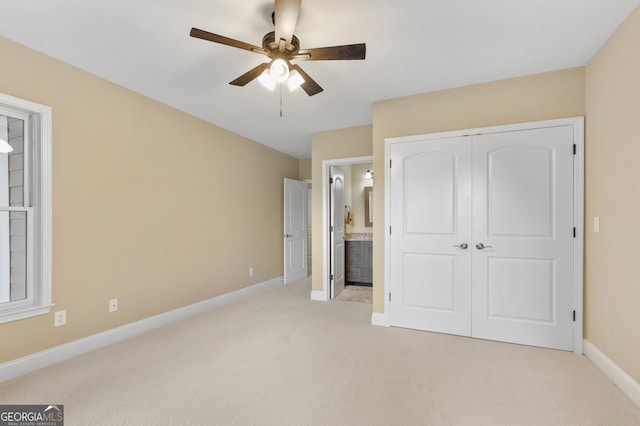 unfurnished bedroom featuring ensuite bathroom, light carpet, ceiling fan, and a closet