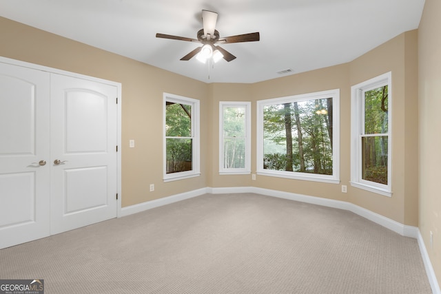 interior space with ceiling fan, multiple windows, light carpet, and a closet